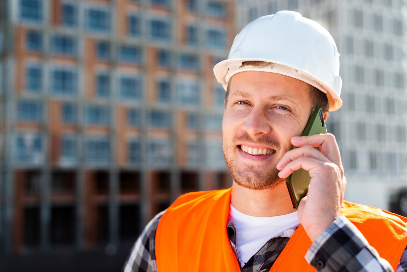 Expert en traitement des remontées capillaires, portant un casque de sécurité et un gilet haute visibilité, consultant un client par téléphone devant un site en construction.